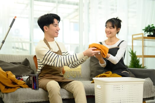 Cheerful young couple folding laundry together in a cozy living room.