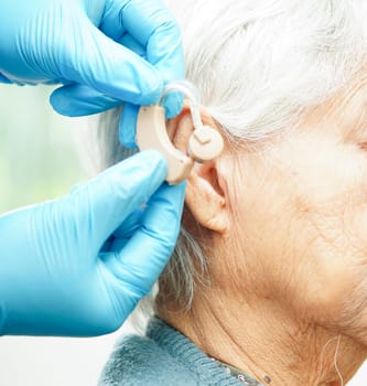 Doctor install hearing aid on senior patient ear to reduce hearing loss problem.