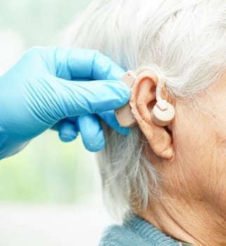 Doctor install hearing aid on senior patient ear to reduce hearing loss problem.