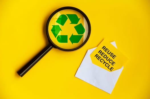 Top view of magnifying glass with recycle symbol and reuse, reduce and recycle text on paper envelope.