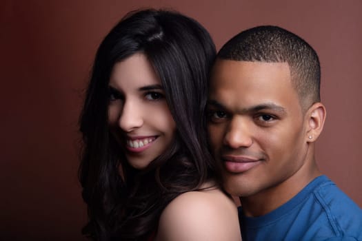Happy, interracial couple smiling and embracing in front of a warm brown background, radiating love and joy in a romantic studio shot