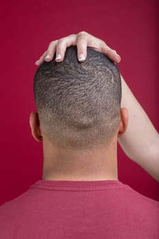 Woman hand gently touching a man's head from behind, creating a sense of intimacy and connection on a vibrant red background