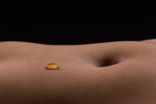 Beautiful seductive young female makes honey on a black background. Drops of honey on her belly.