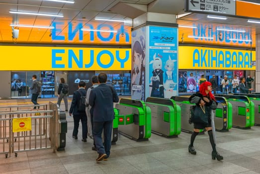 tokyo, akihabara - may 07 2024: Commuters and a cosplayer girl  navigate through the turnstiles of Central Exit the bustling Akihabara station beneath a yellow neon signage written Enjoy Akihabara !