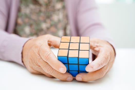 Bangkok, Thailand - May 15, 2022 Asian elderly woman playing Rubik cube game for treatment dementia prevention and Alzheimer disease.