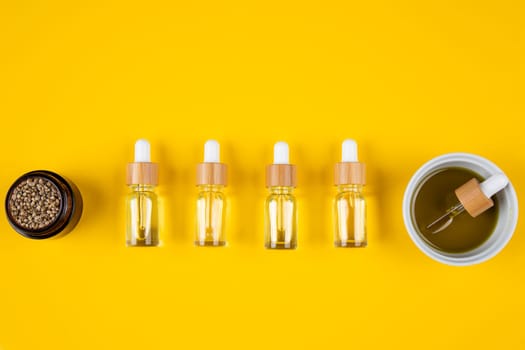 Set of essential oil in a glass bottle, with a pipette on a yellow background, top view