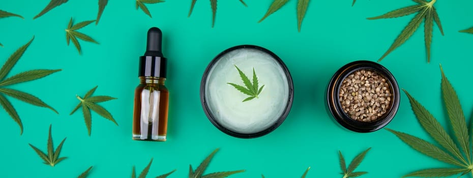 Flat lay composition with hemp oil and hemp leaves on green background