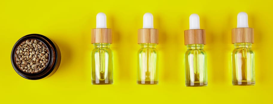 Set of essential oil in a glass bottle, with a pipette on a yellow background, top view
