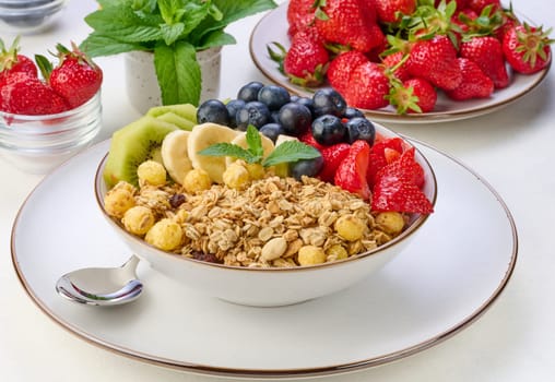 Granola with strawberries, kiwi, banana and blueberries in a round plate on a white table. Healthy and tasty food, top view