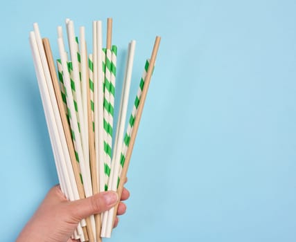 Female hand holding paper cocktail straws on a blue background