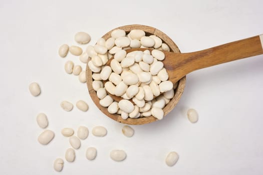 Raw white beans in a plate on the white table, top view.