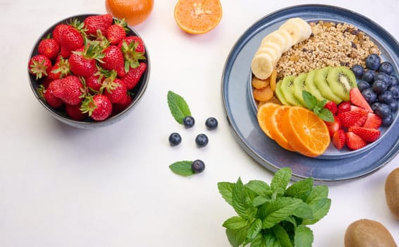 Granola with strawberries, kiwi, banana and blueberries in a round plate on a white table. Healthy and tasty food, top view