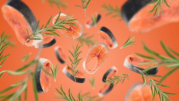 Raw salmon steaks and rosemary sprigs levitate on an orange background