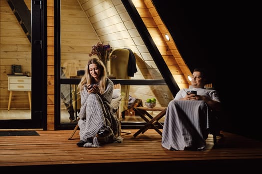 A friendly married couple is sitting on the terrace of log cabin and enjoys warm evening