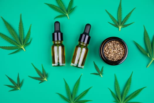 Flat lay composition with hemp oil and hemp leaves on green background
