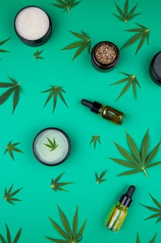 Flat lay composition with hemp oil and hemp leaves on green background