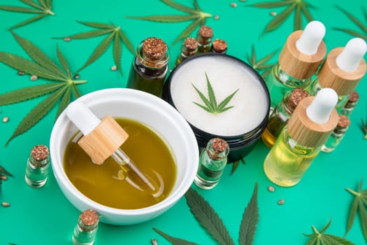 Flat lay composition with hemp oil and hemp leaves on green background