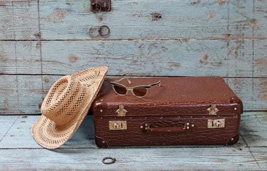 Off on vacation. An old suitcase with a straw hat and sunglasses in front of a wooden background