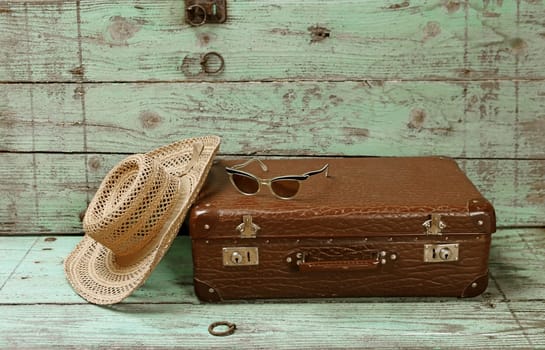 Off on vacation. An old suitcase with a straw hat and sunglasses in front of a wooden background