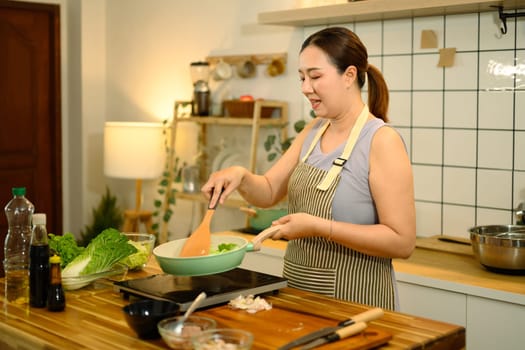 Happy adult woman wearing apron cooking healthy meal in kitchen.