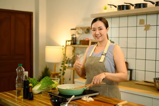 Beautiful woman cooking a delicious meal in her kitchen and gives thumbs up at camera.