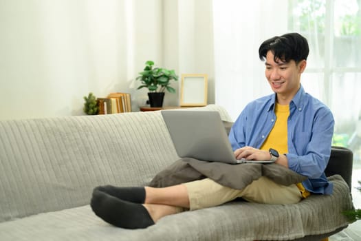 Handsome male freelancer working on laptop while sitting on sofa at home.