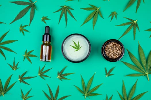Flat lay composition with hemp oil and hemp leaves on green background