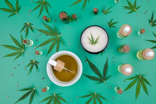 Flat lay composition with hemp oil and hemp leaves on green background