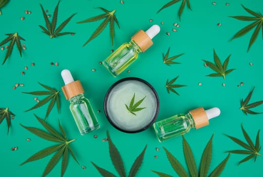 Flat lay composition with hemp oil and hemp leaves on green background