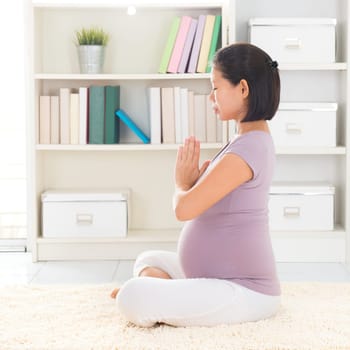 Pregnancy yoga meditation. Full length healthy 8 months pregnant calm Asian woman meditating or doing yoga exercise at home. Relaxation yoga lotus prayer pose.