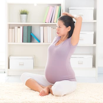 Pregnancy yoga meditation. Full length healthy 8 months pregnant calm Asian woman meditating or doing yoga exercise at home. Relaxation yoga stretching positions.