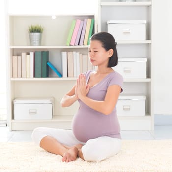 Pregnancy yoga meditation. Full length healthy 8 months pregnant calm Asian woman meditating or doing yoga exercise at home. Relaxation yoga positions.