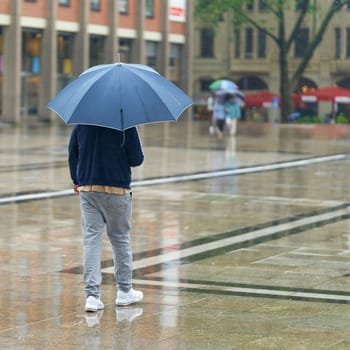 Young man with umbrella in the rain in the city center of Cologne in Germany