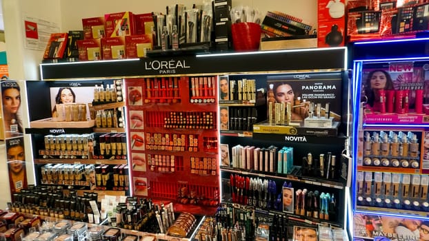 Rimini, Italy - June 25, 2024: Shop window Loreal Paris with women's cosmetics, lipstick, ear, blush, shadows. Season shopping by sale prices. Passing shoppers and passers-by.