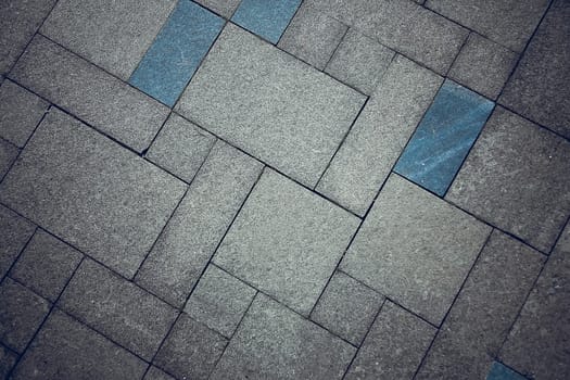 Close-up of a sidewalk with intertwined gray and blue tiles forming a geometric pattern, background image