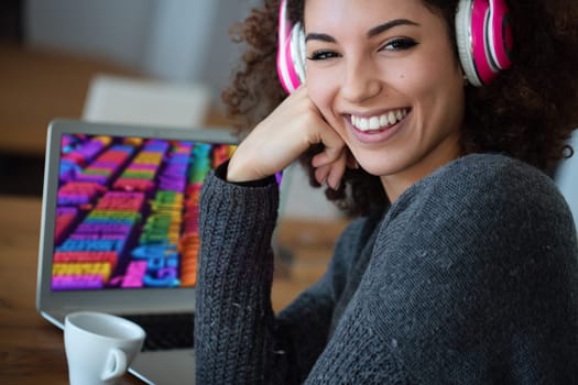 Young woman happily works as a graphic designer in her vibrant home office, smiling as she creates colorful designs on her laptop and sips coffee during breaks