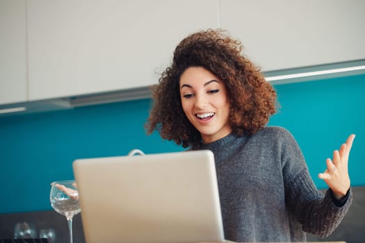 Curly-haired woman in a kitchen gesticulates during a video call, her expression lively and enthusiastic. Her engagement and cheerful demeanor suggest a positive and enjoyable interaction