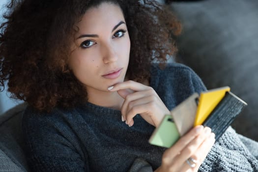 In a cozy living room, a woman with dark curly hair inspects several colorful samples from a furniture store. Her calm, focused demeanor suggests she's carefully planning her interior design choices