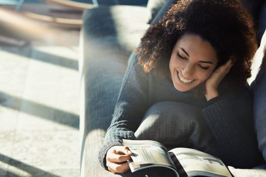 Young woman with curly hair relaxes on her couch, reading a magazine in her cozy living room, enjoying a carefree day at home