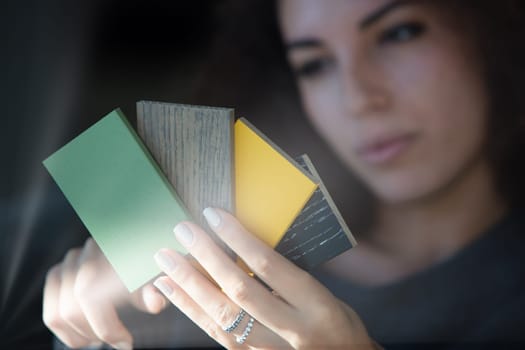 With curly hair and a contemplative look, the woman reviews different color samples in her living room. Her precise attention indicates she's selecting hues for furniture, showing a keen eye for detai