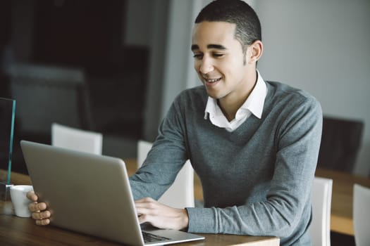 Young man happily works from home, typing on a laptop in a cozy office setup, showing dedication