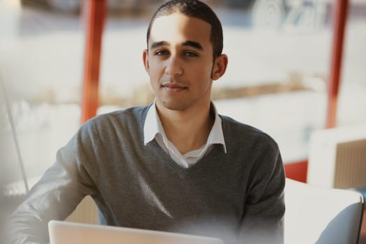 Young man works comfortably from his home office, sitting by the window with his laptop, enjoying natural daylight