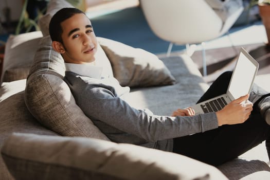 Young professional is working remotely, comfortably seated on a couch in a modern home office, using a laptop with a blank screen