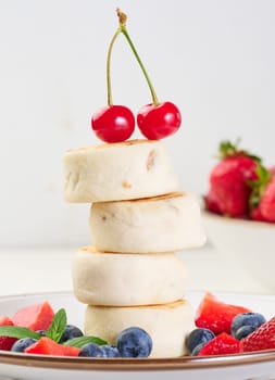 A stack of four cheesecakes on a plate with berries, blueberries, strawberries and cherries. Background white