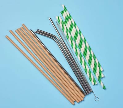 Disposable paper straws and metal cocktail straws on blue background, top view