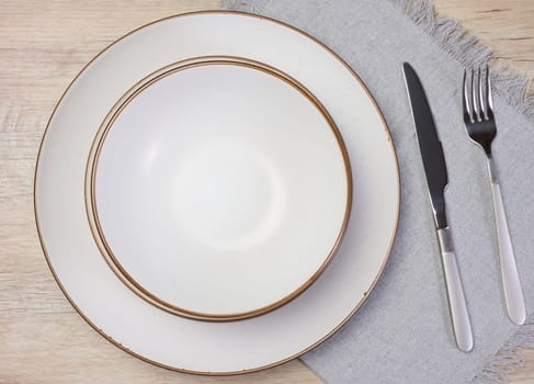Round empty white ceramic plate, knife and fork on the table, top view