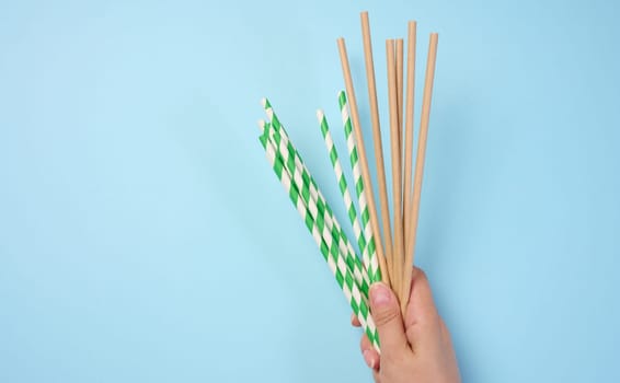 Female hand holding paper cocktail straws on a blue background