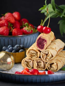 Crepes stacked in a pile, one of which is cut and filled with berry filling, close up
