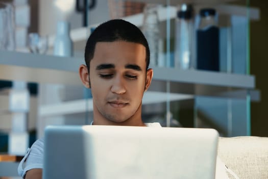 Young man on a cozy sofa uses a laptop at home, focused and deep in thought, representing the digital nomad lifestyle of millennials and gen z