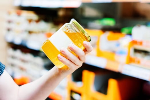 Young male hand holds honey on a blurred background, row of shelves with groceries in supermarket